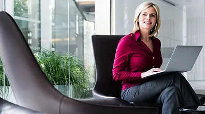 A woman sitting in a chair while using a laptop that is resting on her crossed legs 